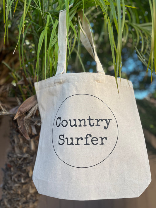 A beige cotton tote bag with 'Country Surfer' printed in black text on the front.